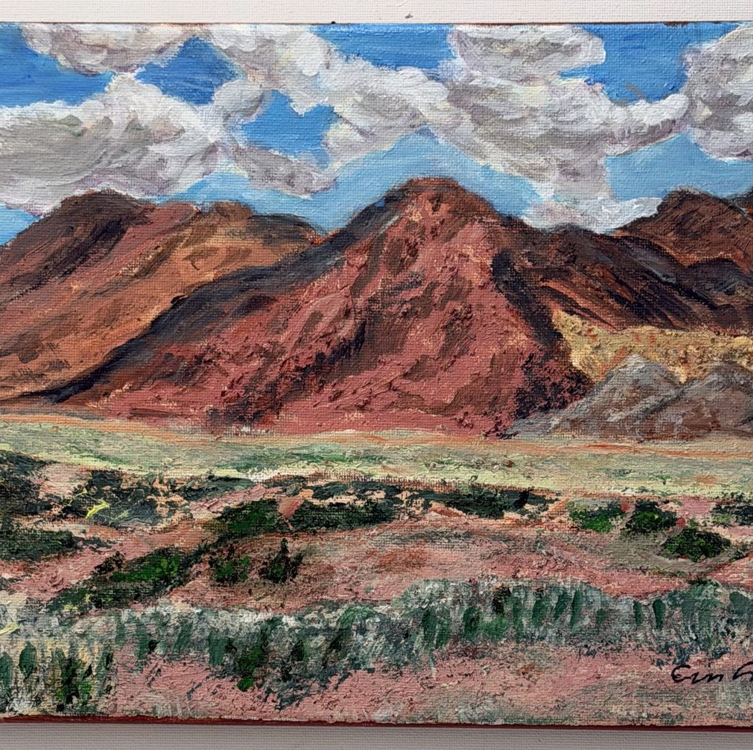 Painting of red mountains over a desert valley under white clouds